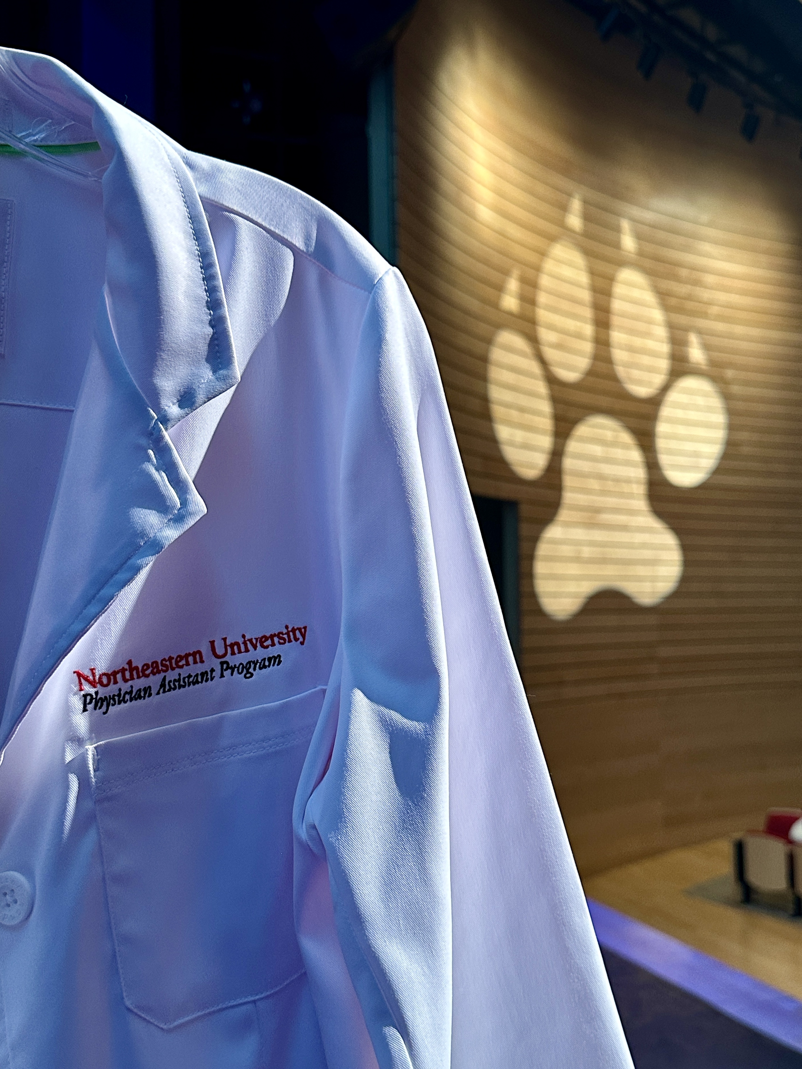 A photo of a PA student white coat with a husky paw projected on the wall in the background.